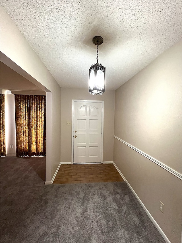 carpeted entrance foyer with a textured ceiling and a chandelier