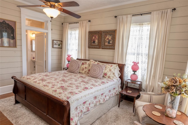 bedroom with crown molding, wooden walls, ceiling fan, and hardwood / wood-style flooring