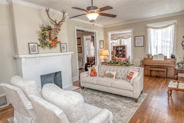 living room with ceiling fan, a brick fireplace, a textured ceiling, crown molding, and hardwood / wood-style floors