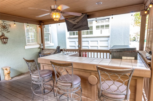 wooden deck with a wet bar, ceiling fan, and area for grilling