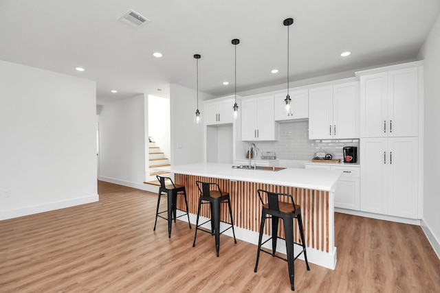 kitchen featuring pendant lighting, a kitchen island with sink, white cabinets, light hardwood / wood-style floors, and a breakfast bar area