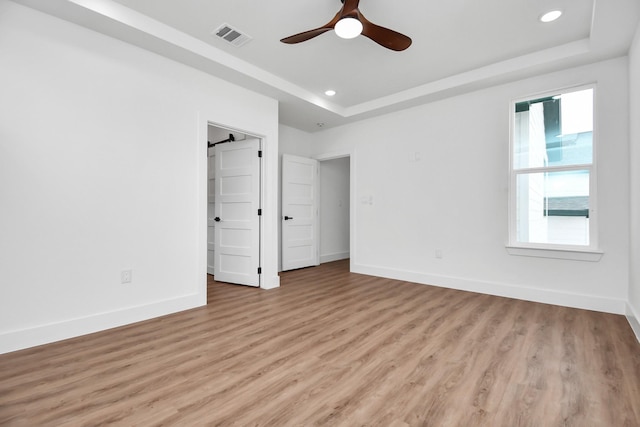 unfurnished bedroom featuring a tray ceiling, ceiling fan, and light hardwood / wood-style floors