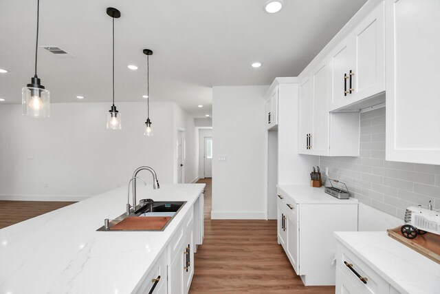 kitchen featuring light stone counters, sink, pendant lighting, hardwood / wood-style flooring, and white cabinetry