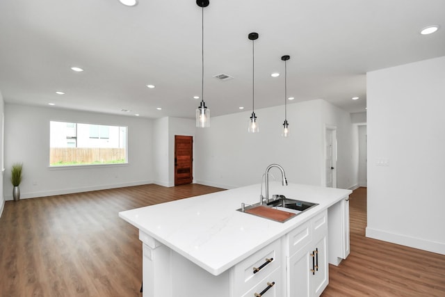 kitchen featuring white cabinetry, sink, pendant lighting, a kitchen island with sink, and light wood-type flooring