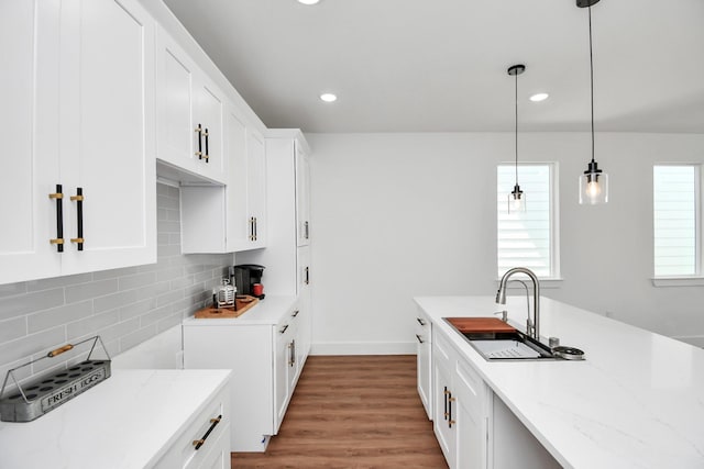 kitchen with backsplash, sink, hanging light fixtures, light stone counters, and white cabinetry