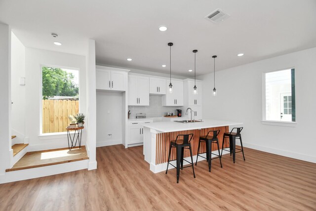 kitchen with white cabinetry, sink, an island with sink, pendant lighting, and a breakfast bar