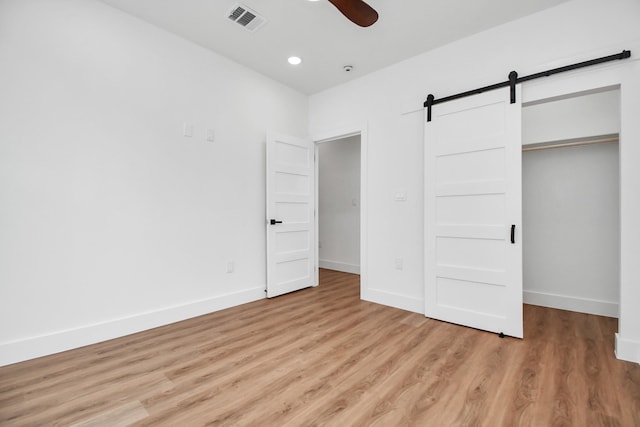 unfurnished bedroom with light wood-type flooring, a barn door, a closet, and ceiling fan