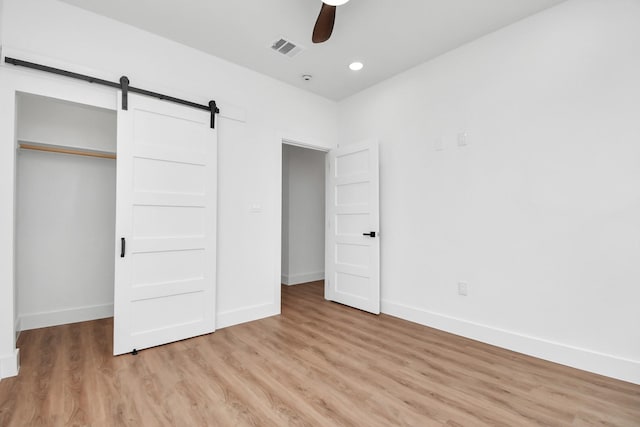 unfurnished bedroom featuring a barn door, a closet, light hardwood / wood-style flooring, and ceiling fan