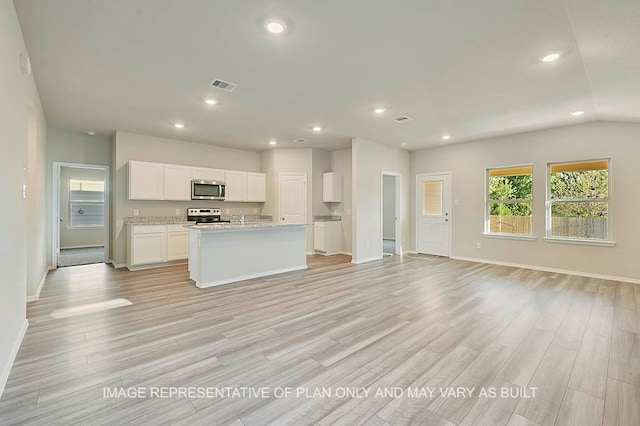 kitchen with light stone counters, light wood-type flooring, appliances with stainless steel finishes, an island with sink, and white cabinets