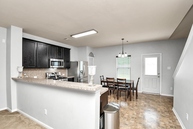 kitchen featuring hanging light fixtures, kitchen peninsula, tasteful backsplash, stainless steel appliances, and an inviting chandelier