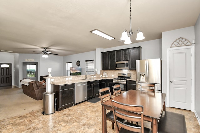 kitchen featuring sink, ceiling fan with notable chandelier, kitchen peninsula, appliances with stainless steel finishes, and decorative light fixtures