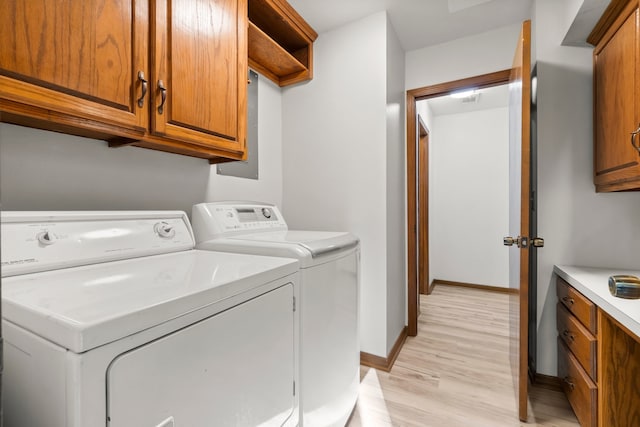 washroom featuring washer and clothes dryer, light hardwood / wood-style flooring, and cabinets