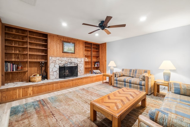 living room with a stone fireplace, hardwood / wood-style floors, built in features, and ceiling fan