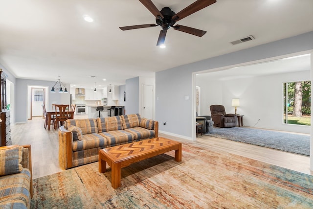 living room featuring ceiling fan with notable chandelier and light wood-type flooring