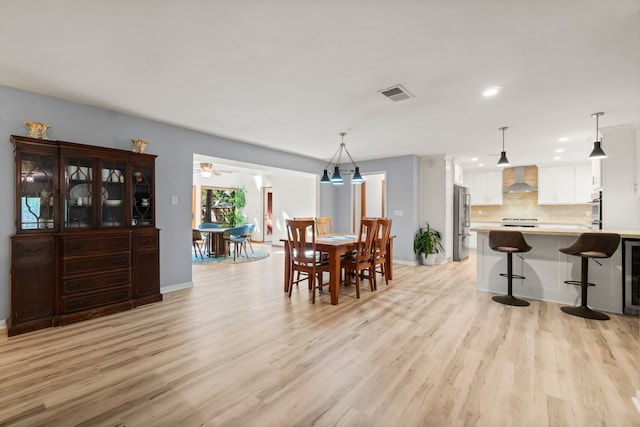 dining space with ceiling fan, wine cooler, and light wood-type flooring