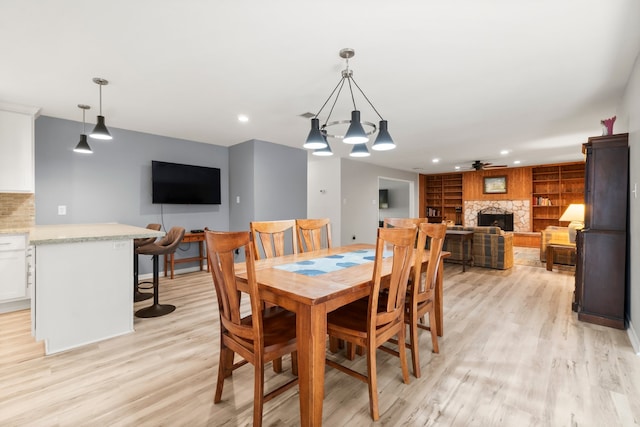 dining space featuring a stone fireplace, light hardwood / wood-style flooring, and ceiling fan with notable chandelier