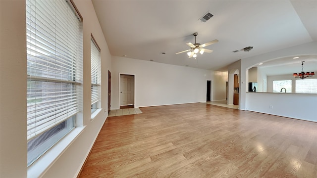 unfurnished living room with ceiling fan with notable chandelier and light hardwood / wood-style flooring