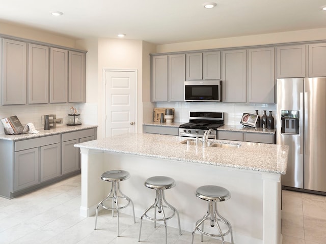 kitchen featuring stainless steel appliances, light stone counters, a center island with sink, and sink