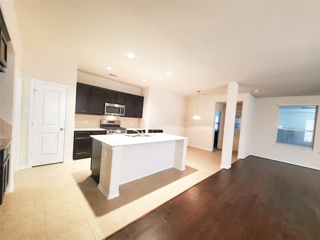 kitchen featuring hanging light fixtures, sink, a center island with sink, light hardwood / wood-style flooring, and appliances with stainless steel finishes