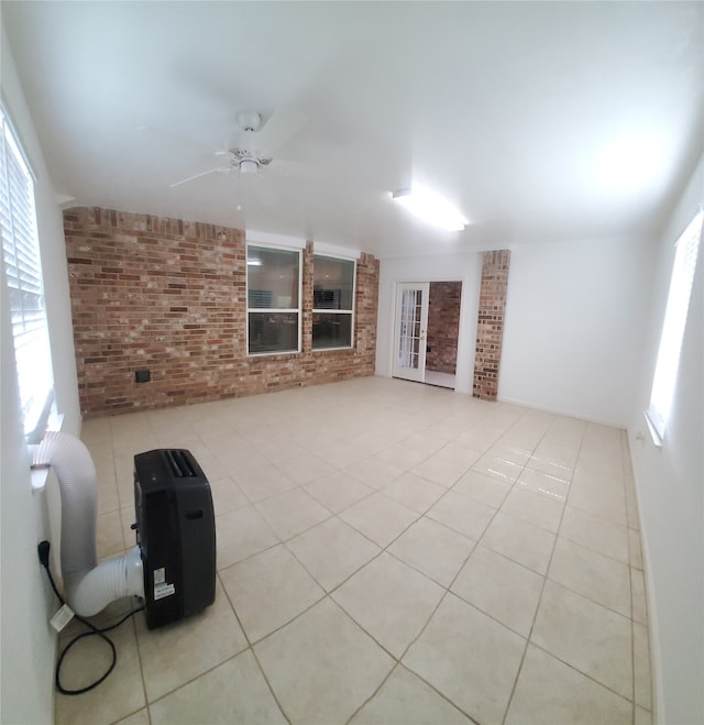 unfurnished living room with ceiling fan, brick wall, and light tile patterned floors