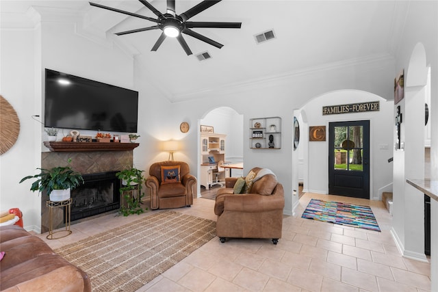 living room featuring light tile patterned flooring, vaulted ceiling, a tiled fireplace, crown molding, and ceiling fan