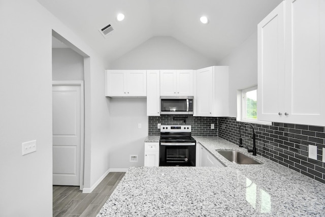 kitchen with sink, light stone countertops, stainless steel appliances, and vaulted ceiling