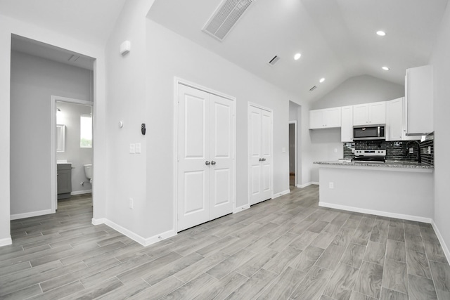 kitchen with light stone countertops, stainless steel appliances, light hardwood / wood-style flooring, white cabinets, and lofted ceiling