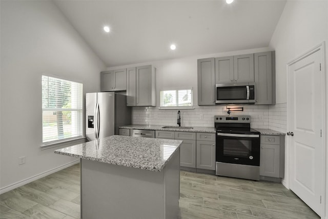 kitchen featuring sink, a kitchen island, stainless steel appliances, gray cabinets, and light stone counters