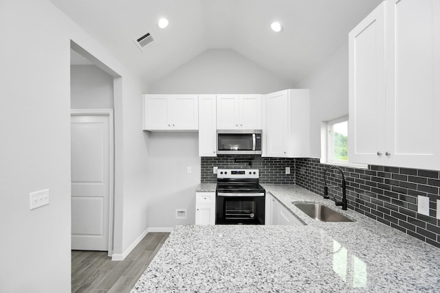 kitchen featuring lofted ceiling, stainless steel appliances, sink, and light stone counters