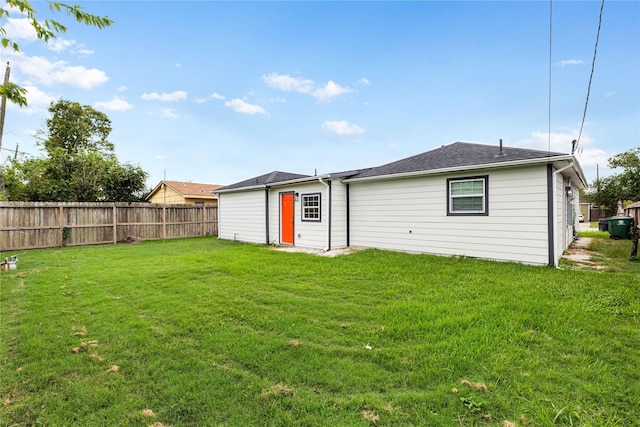 rear view of property featuring a lawn and fence