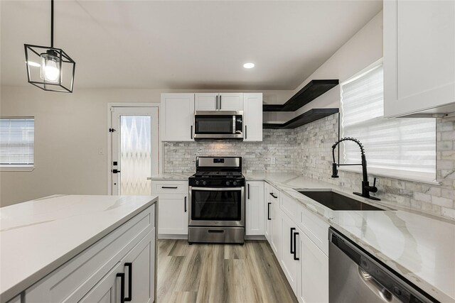 kitchen with appliances with stainless steel finishes, light stone counters, sink, white cabinetry, and hanging light fixtures