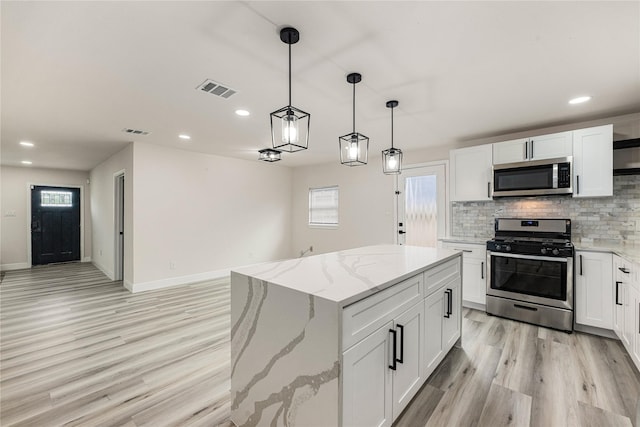 kitchen with decorative backsplash, white cabinets, appliances with stainless steel finishes, light stone countertops, and light wood-type flooring