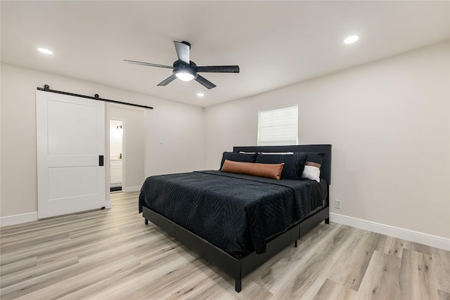 bedroom featuring light wood finished floors, a barn door, and baseboards