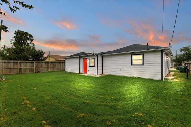 back house at dusk featuring a lawn