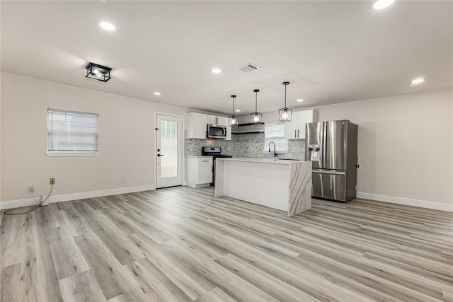 kitchen with white cabinets, a center island with sink, sink, hanging light fixtures, and stainless steel appliances