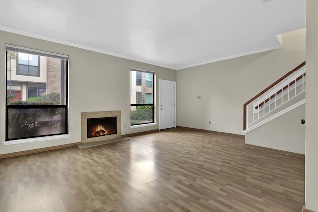 unfurnished living room with ornamental molding, wood-type flooring, a high end fireplace, and a healthy amount of sunlight