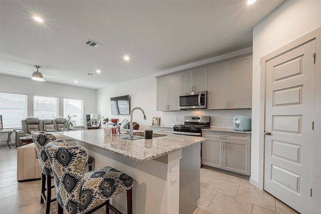 kitchen featuring a center island with sink, gray cabinetry, ceiling fan, and stainless steel appliances