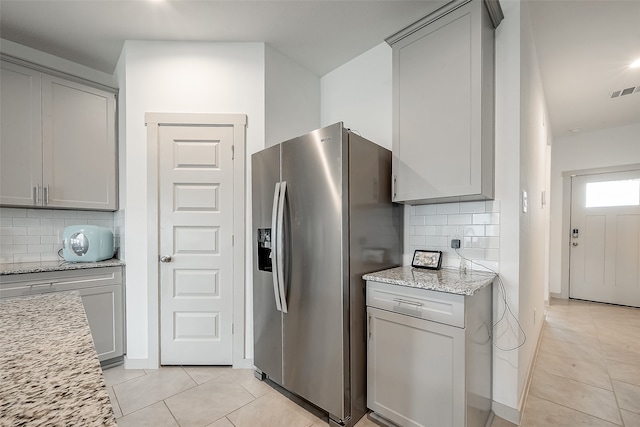 kitchen with decorative backsplash, gray cabinetry, light stone countertops, and stainless steel fridge with ice dispenser