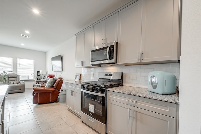 kitchen featuring appliances with stainless steel finishes, decorative backsplash, light stone counters, light tile patterned floors, and gray cabinets