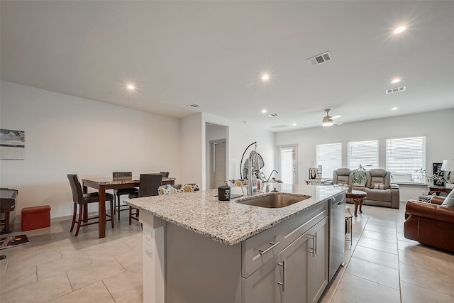 kitchen with light stone countertops, ceiling fan, stainless steel dishwasher, a kitchen island with sink, and sink