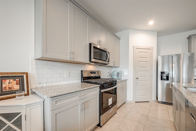 kitchen featuring gray cabinets, stainless steel appliances, backsplash, light tile patterned floors, and light stone countertops