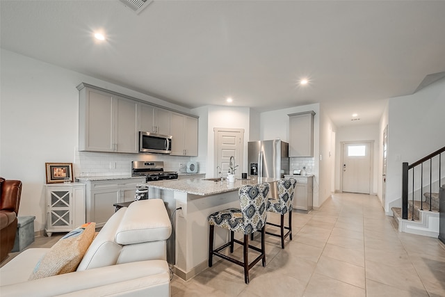 kitchen featuring gray cabinets, a center island with sink, a breakfast bar area, and stainless steel appliances