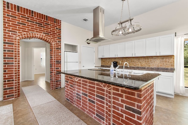 kitchen featuring an island with sink, white cabinetry, white refrigerator, and island range hood