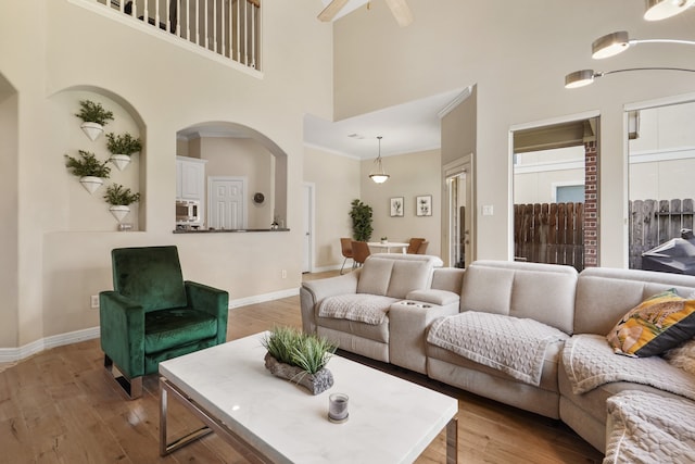 living room featuring ceiling fan, light hardwood / wood-style flooring, crown molding, and a high ceiling