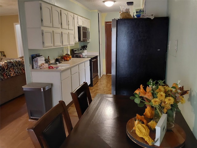 kitchen featuring a textured ceiling, appliances with stainless steel finishes, light parquet floors, and white cabinetry