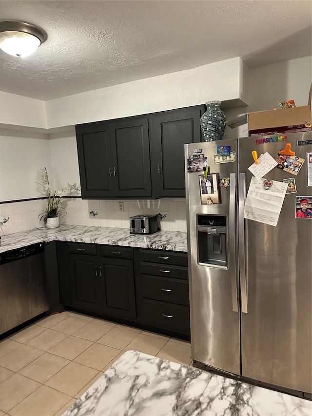 kitchen featuring a textured ceiling, light tile patterned flooring, backsplash, appliances with stainless steel finishes, and light stone countertops