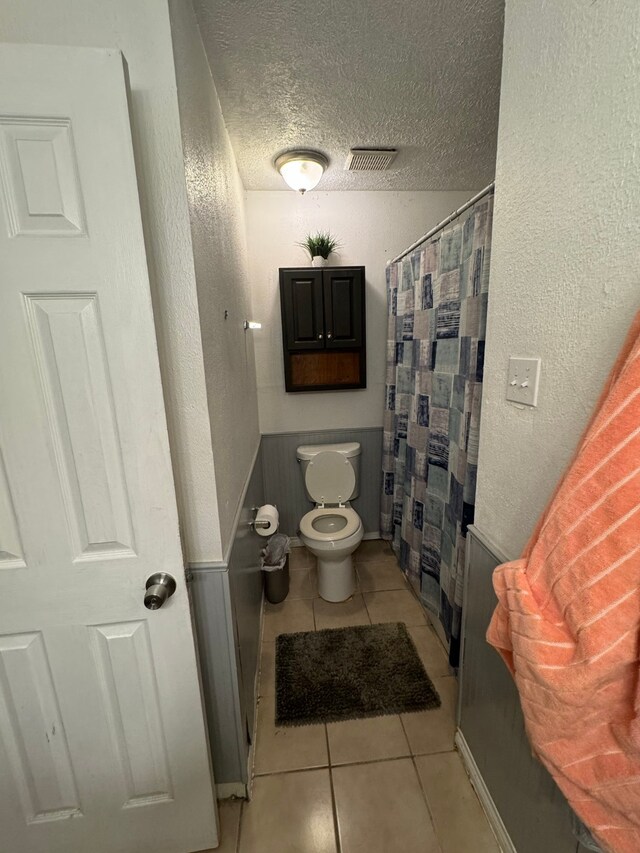 bathroom featuring a shower with curtain, a textured ceiling, toilet, and tile patterned floors