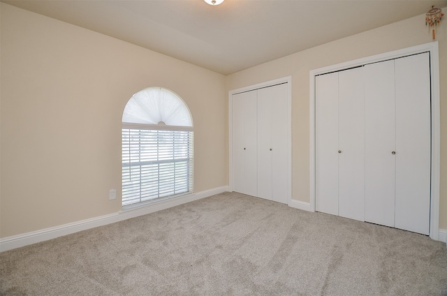 unfurnished bedroom featuring two closets and light carpet