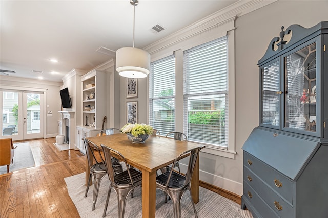 dining area with crown molding, light wood-type flooring, and french doors