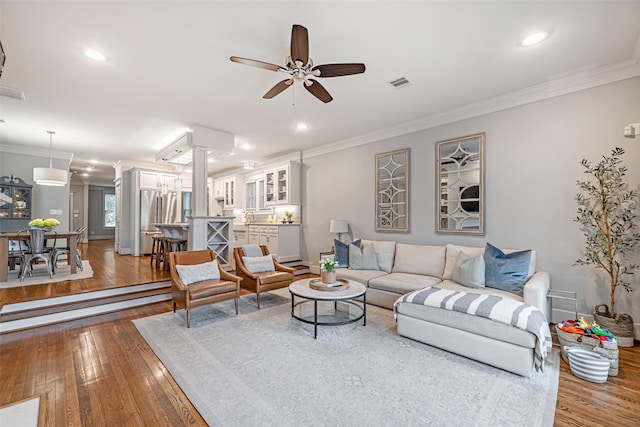 living room featuring decorative columns, crown molding, hardwood / wood-style flooring, and ceiling fan